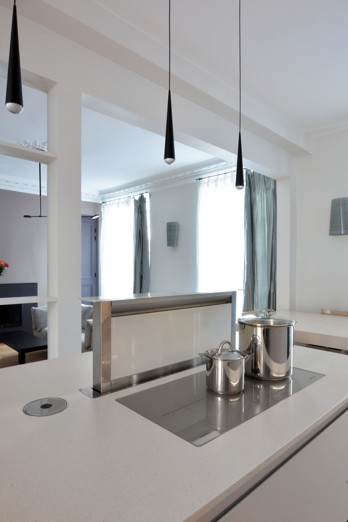 Îlot central de cuisine blanc avec suspensions noires, plaque cuisson et plan minéral — appartement Paris 6e