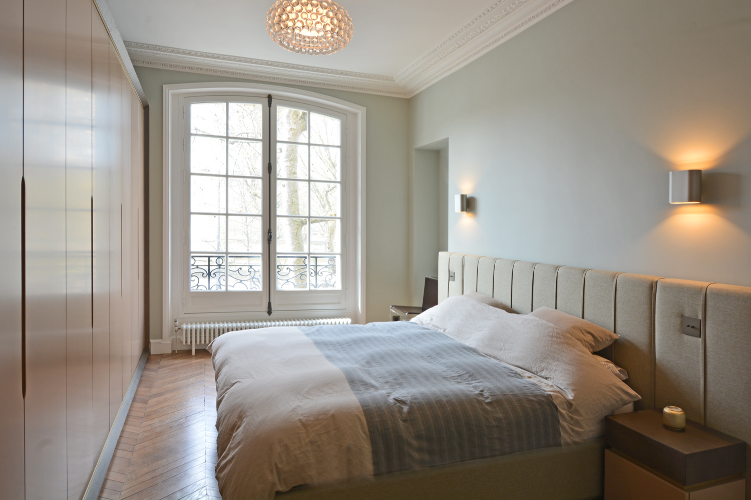 Chambre parentale haussmannienne avec dressing laqué, tête de lit capitonnée et fenêtre cintrée — Paris 4e